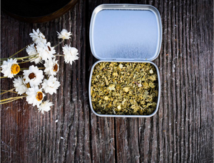 An open tin of Ritual Aromatics Purification Loose Incense on weathered wood with white flowers