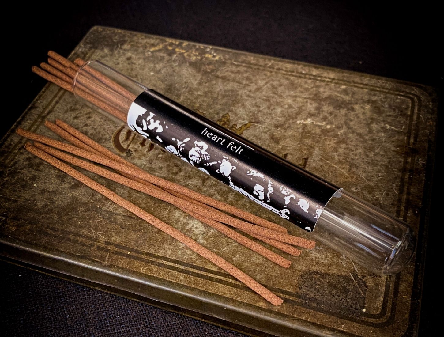 An open glass vial of Ritual Aromatics Heart Felt Japanese Incense Sticks on a vintage cigar case